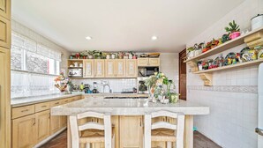 A kitchen with wooden cabinets, a central island, and a variety of decorative items on shelves. - Boutique Hacienda Design and Comfort (Juriquilla)