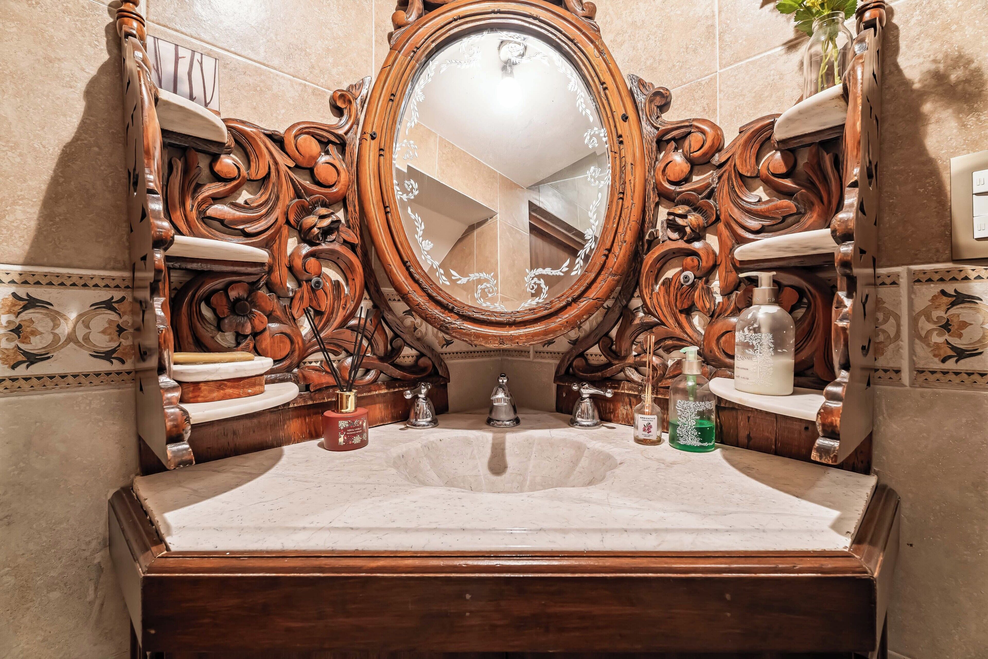 Un baño con un tocador de madera decorativo, un espejo grande y un lavamanos de mármol.