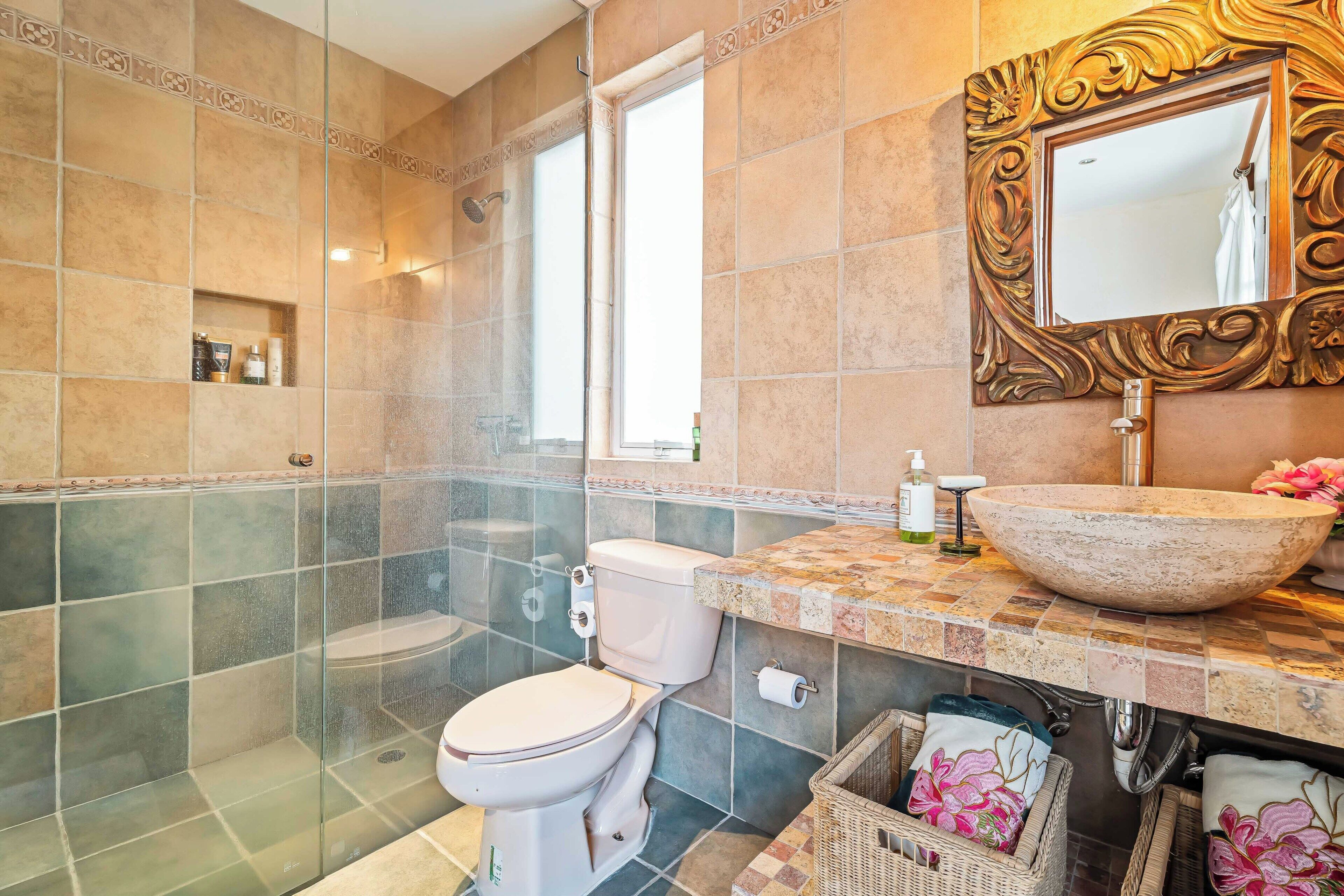 Une salle de bain dotée d’une douche à parois de verre, de toilettes, d’un lavabo avec un grand bac et d’un miroir aux détails ouvragés.