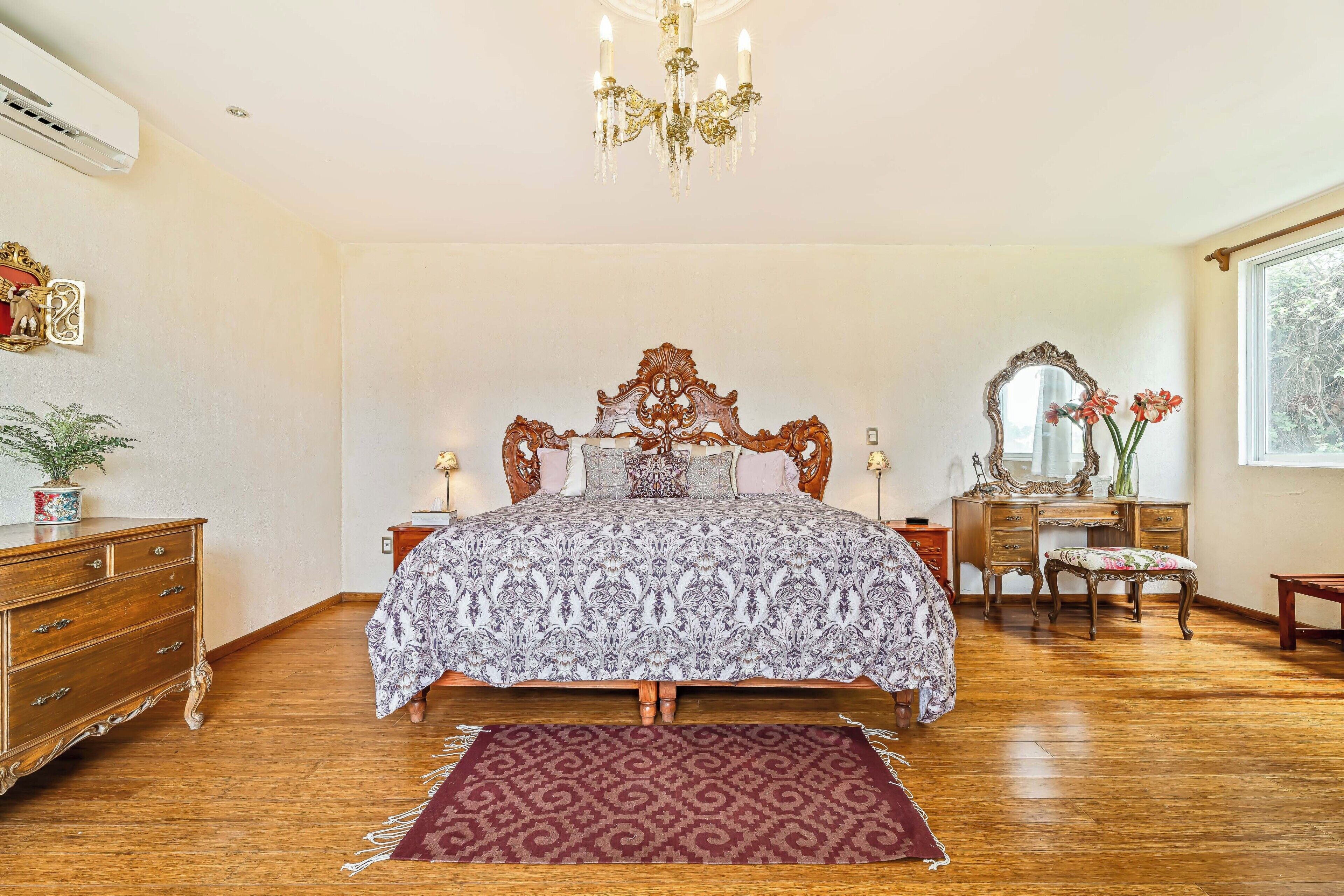 Ein Schlafzimmer mit einem großen Bett, einem hölzernen Schminktisch, einer Kommode und einem Kronleuchter.