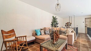 A living room with a wooden rocking chair, a beige sofa, a glass coffee table, and a patterned rug. - Boutique Hacienda Design and Comfort (Juriquilla)