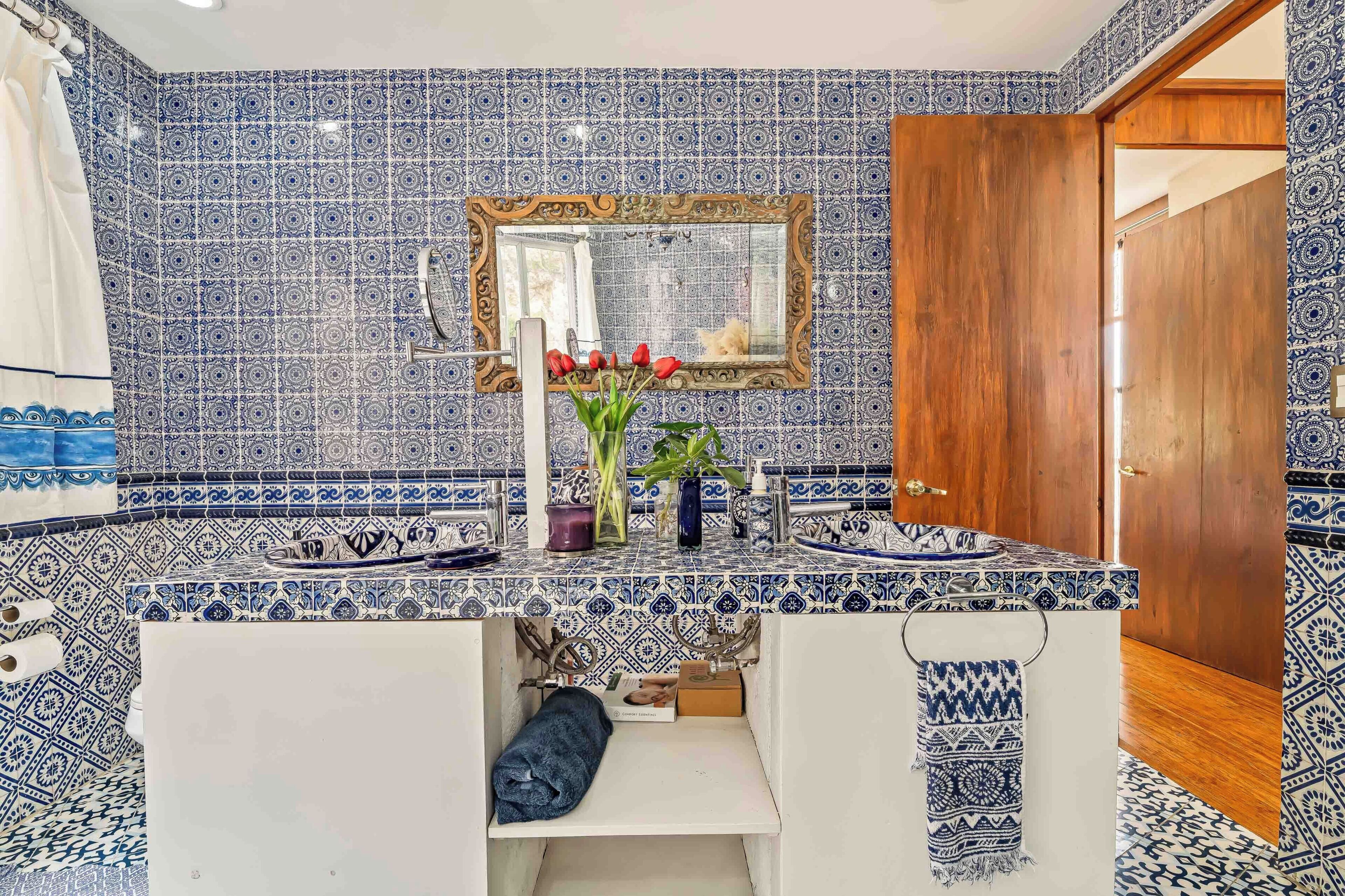 Un baño con baldosas blancas y azules estampadas, una puerta de madera y un espejo con marco decorativo.