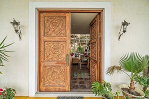 A wooden double door with intricate carvings, a small table with chairs, and potted plants.