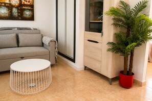A living room with a grey sofa, a white round table, a wooden cabinet, and a potted plant. - Pink Zenn Lodging (Torrevieja)