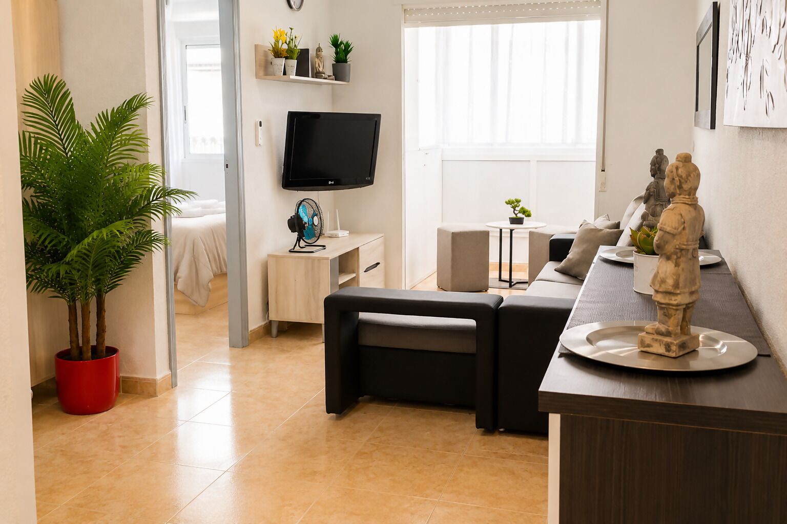 Een moderne woonkamer met een flatscreen televisie, een rode plant in pot, een bank, een kleine tafel met een plant en een beeld op een dienblad.