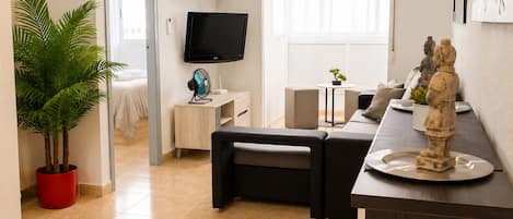Een moderne woonkamer met een flatscreen televisie, een rode plant in pot, een bank, een kleine tafel met een plant en een beeld op een dienblad.