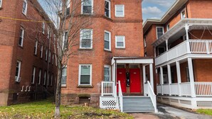 A brick building with a red door and white railings, featuring a small porch and steps leading to the entrance. - The Red Door Retreat - Walking Distance to Downtown Hartford (Hartford)