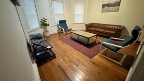 A living room with a brown leather sofa, two blue armchairs, a wooden coffee table, and a potted plant. - The Red Door Retreat - Walking Distance to Downtown Hartford (Hartford)