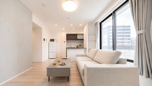 A modern living room with a sofa, coffee table, and a view of the city through large windows. - Three bedroom  in Japan, Taito City (Taito City)
