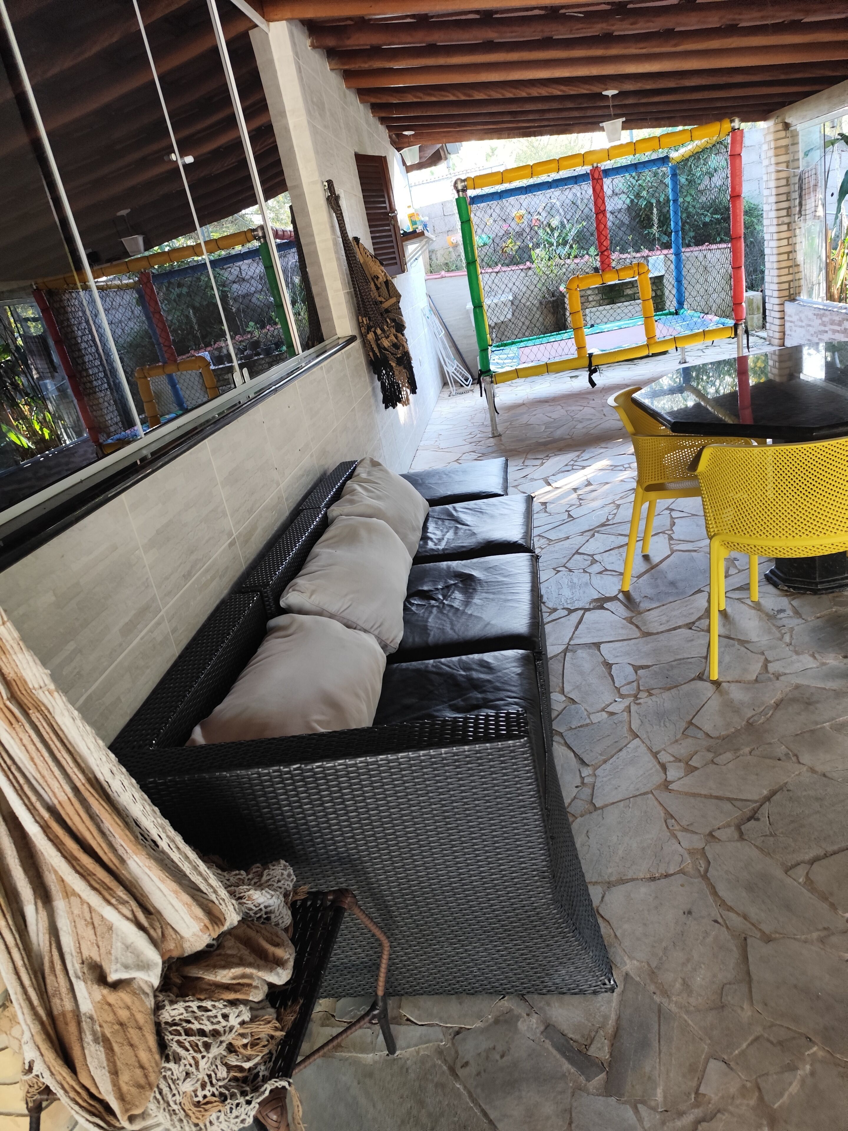 Ein überdachter Außenbereich mit einer Sitzecke, einem Sofa, einem Tisch, Steinböden und Blick ins Freie.