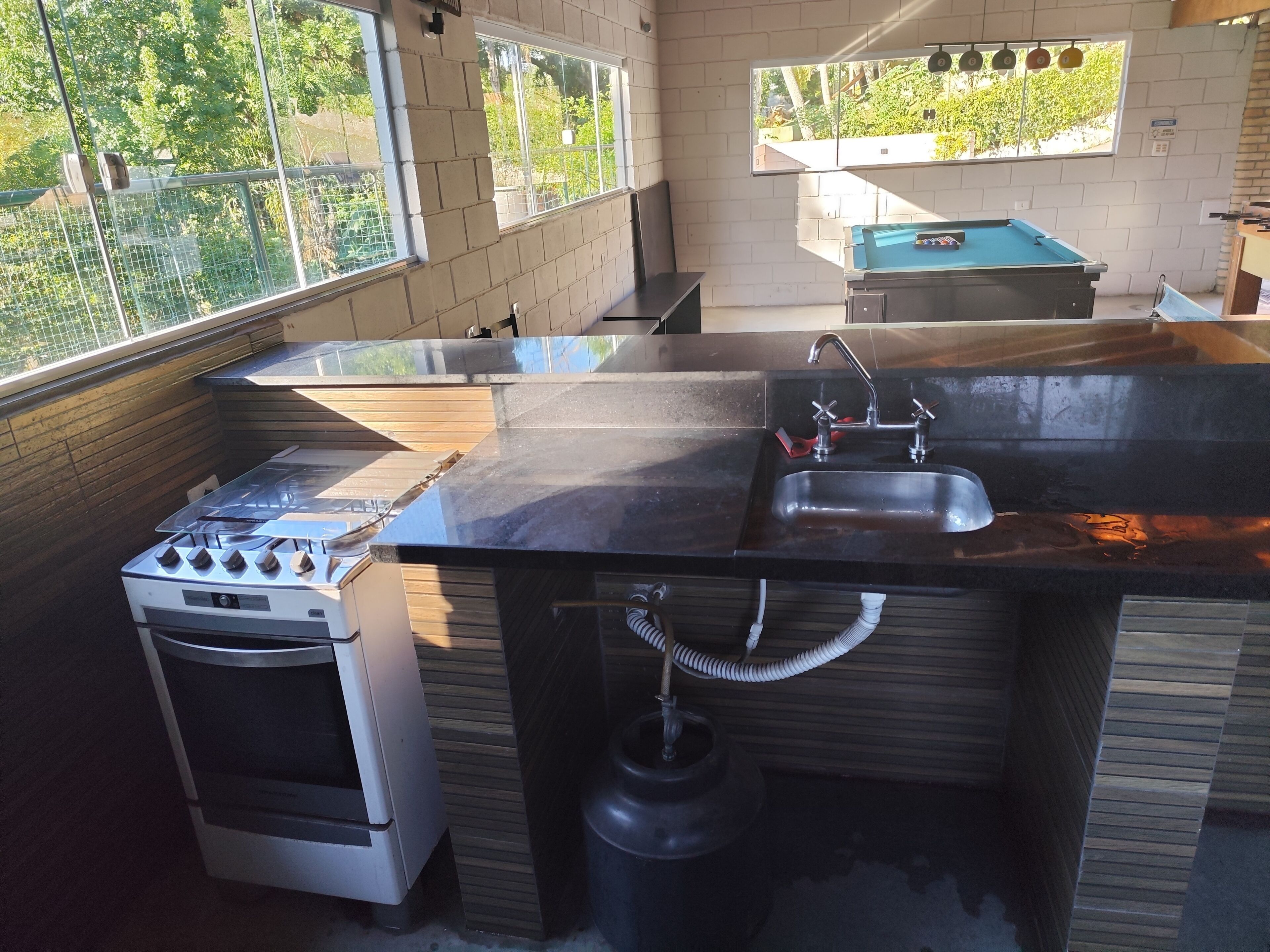 A kitchen with a gas stove, sink, and a view through large windows.