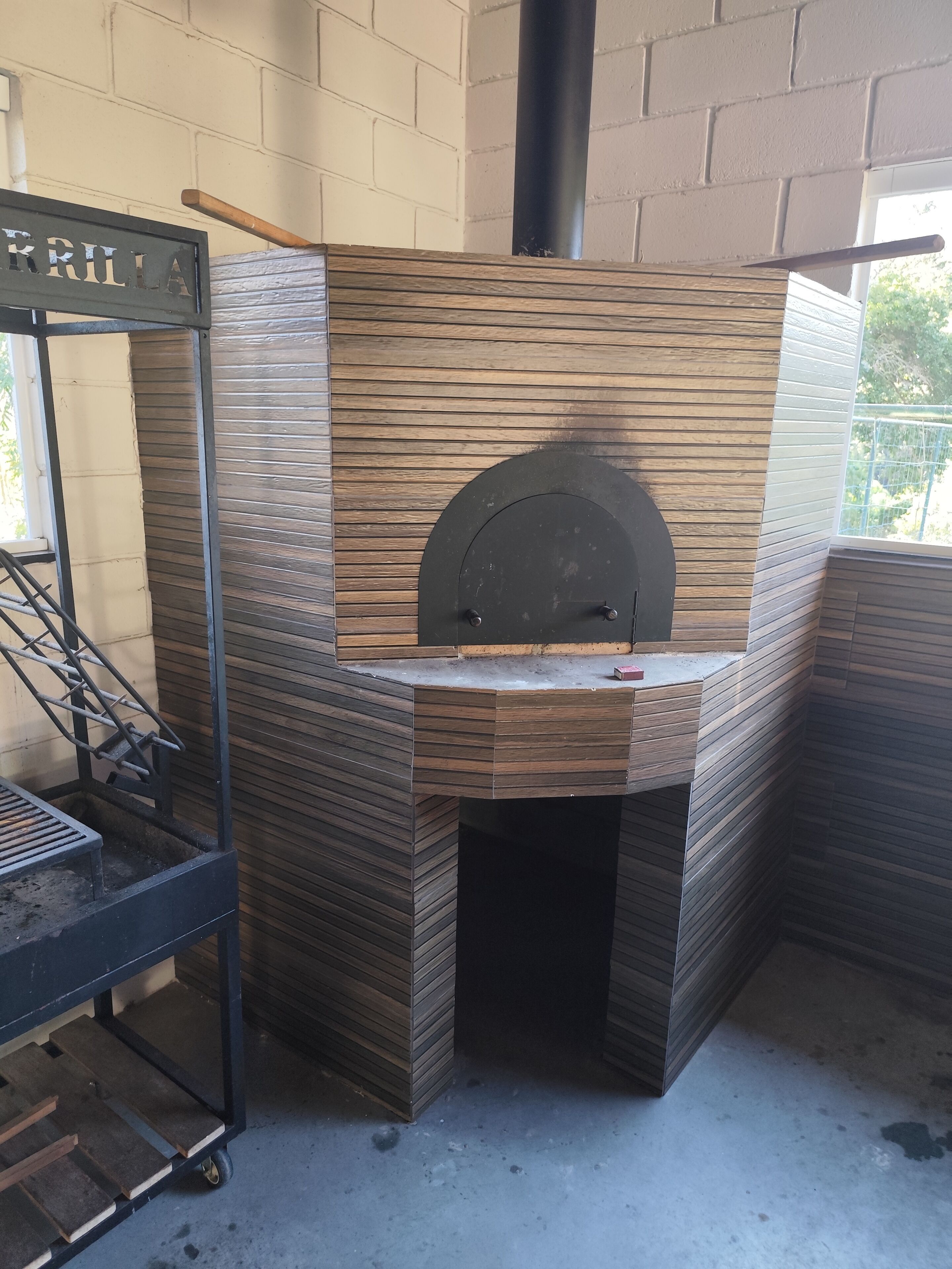 A brick oven with a wooden interior, a metal rack, and a sign that reads 'PIZZA'.