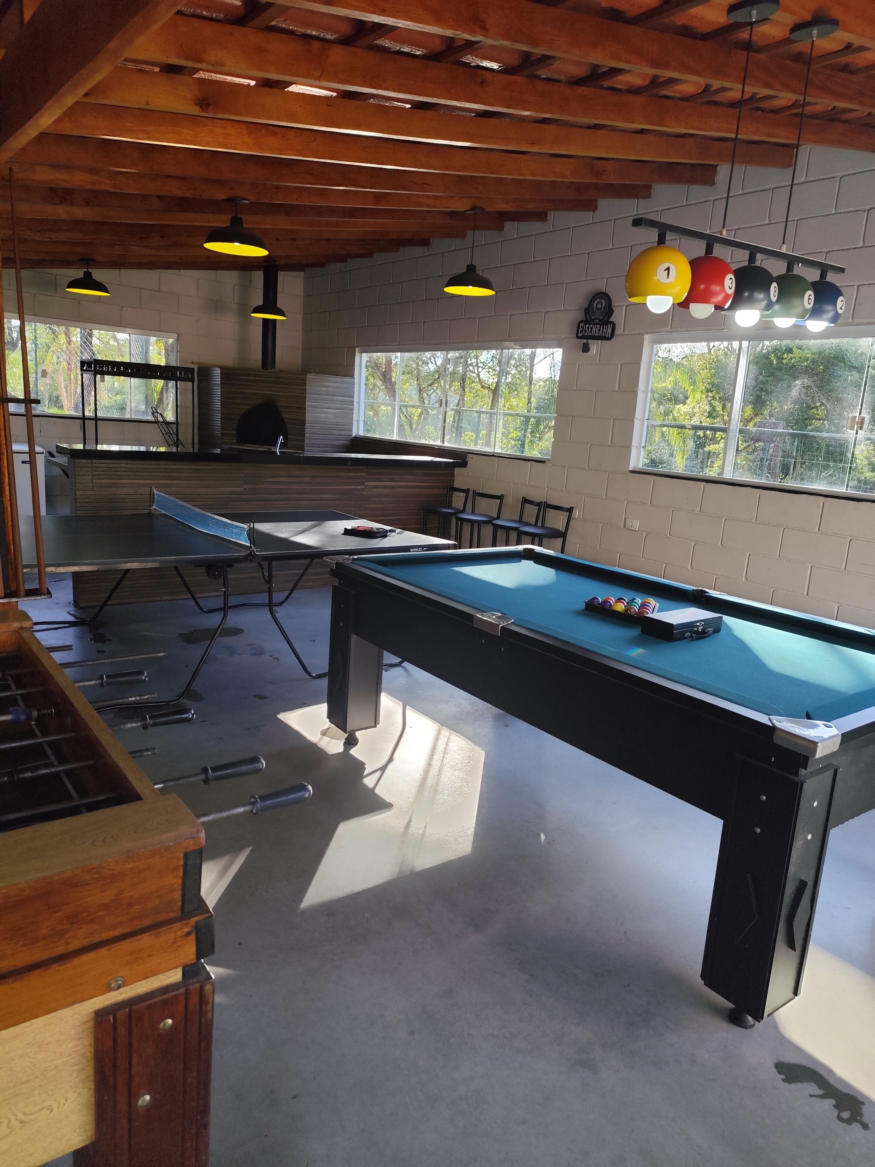 Una mesa de billar con un soporte para tacos, una mesa de futbolín y una zona de bar con taburetes.