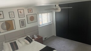 Een slaapkamer met een bed, een nachtkastje, een raam met jaloezieën en wanddecoratie.