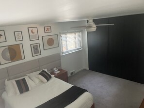 A bedroom with a bed, a nightstand, a window with blinds, and wall art. - Beautiful Mid-Century Oasis in South Shore. (Chicago)