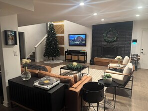 A modern living room with a fireplace, a Christmas tree, and a television. - Beautiful Mid-Century Oasis in South Shore. (Chicago)