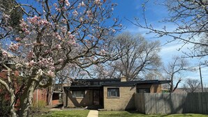 Een klein huis met voortuin, houten omheining en een boom met roze bloesems.