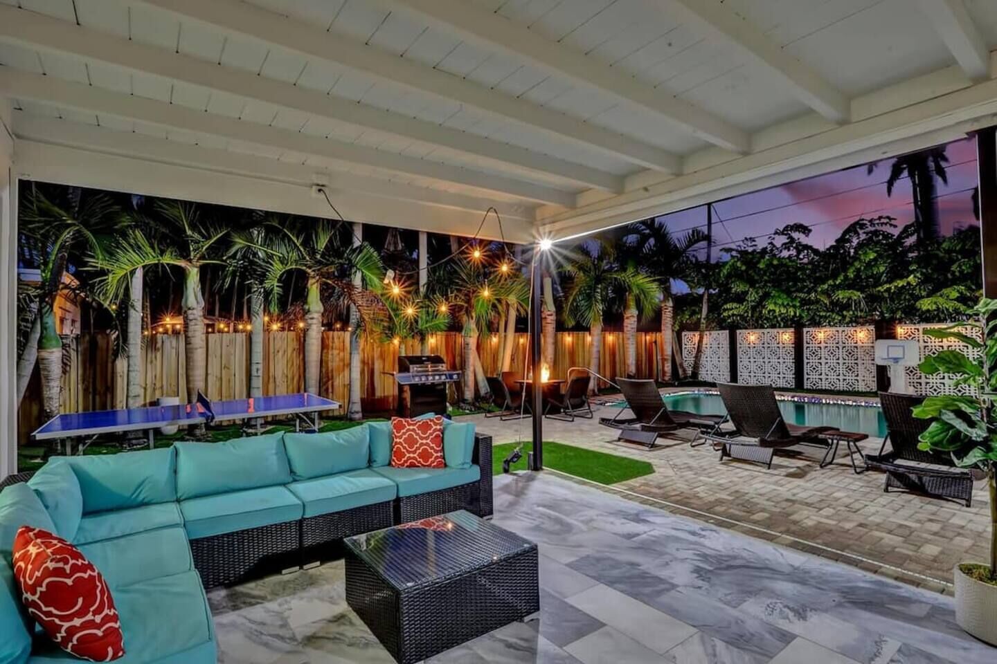 An outdoor patio with a sofa, chairs, a table, a ping pong table, and a barbecue grill.
