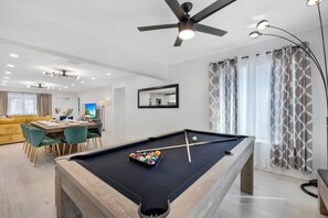 Ein modernes Wohnzimmer mit Billardtisch, einer Couch und einem Essbereich.
