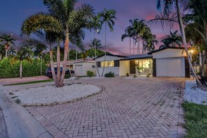 A modern house with a paved driveway, palm trees, and a garage. - Spacious 5BR Heated Pool Villa · minutes to Beach (Hollywood)
