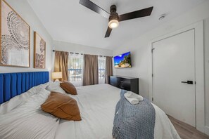 A hotel room with a bed, a ceiling fan, a TV, and a door. - Spacious 5BR Heated Pool Villa · minutes to Beach (Hollywood)