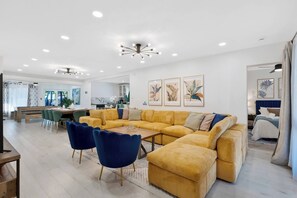 A modern living room with a large sofa, a dining area, and a kitchen in the background. - Spacious 5BR Heated Pool Villa · minutes to Beach (Hollywood)