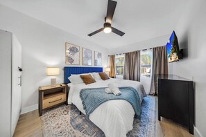 A hotel room with a bed, a ceiling fan, a TV, and a window with curtains. - Spacious 5BR Heated Pool Villa · minutes to Beach (Hollywood)