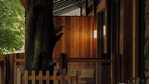 Una cabaña de madera con una bañera grande, una valla de madera y un árbol.