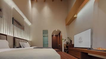 Habitación de hotel moderna con una cama grande, televisor, banca de madera y chimenea empotrada.