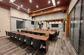 Una sala de conferencias con una larga mesa, sillas, una pantalla de proyector y una pizarra.