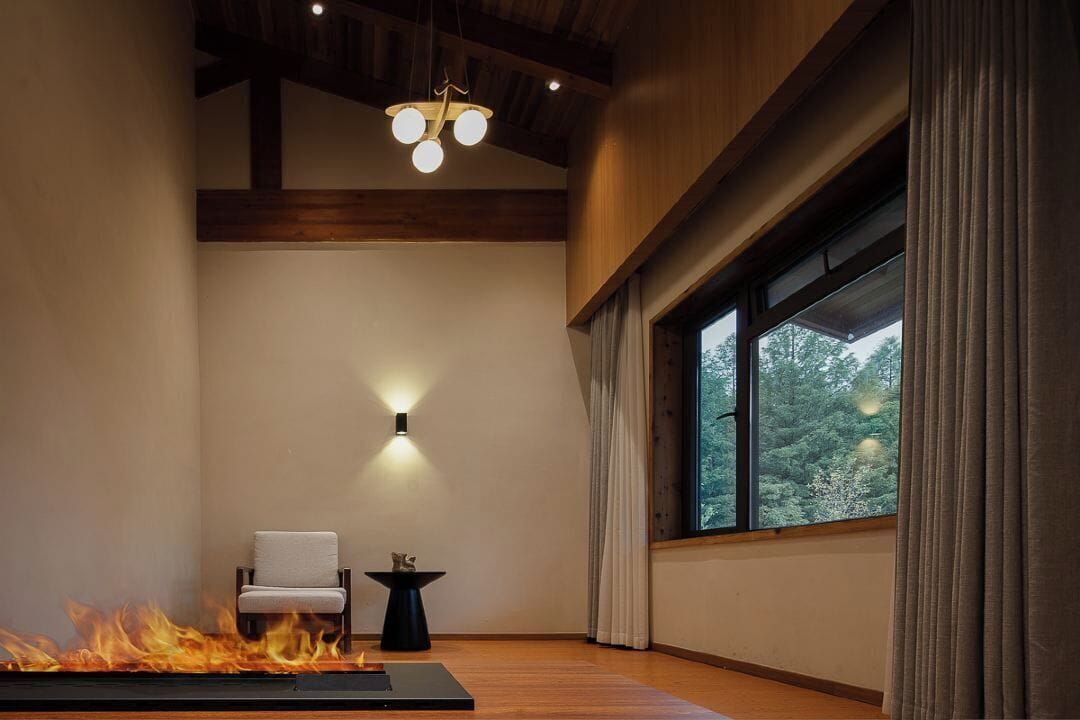 A room with a fireplace, a chair, a table, and a window with curtains.