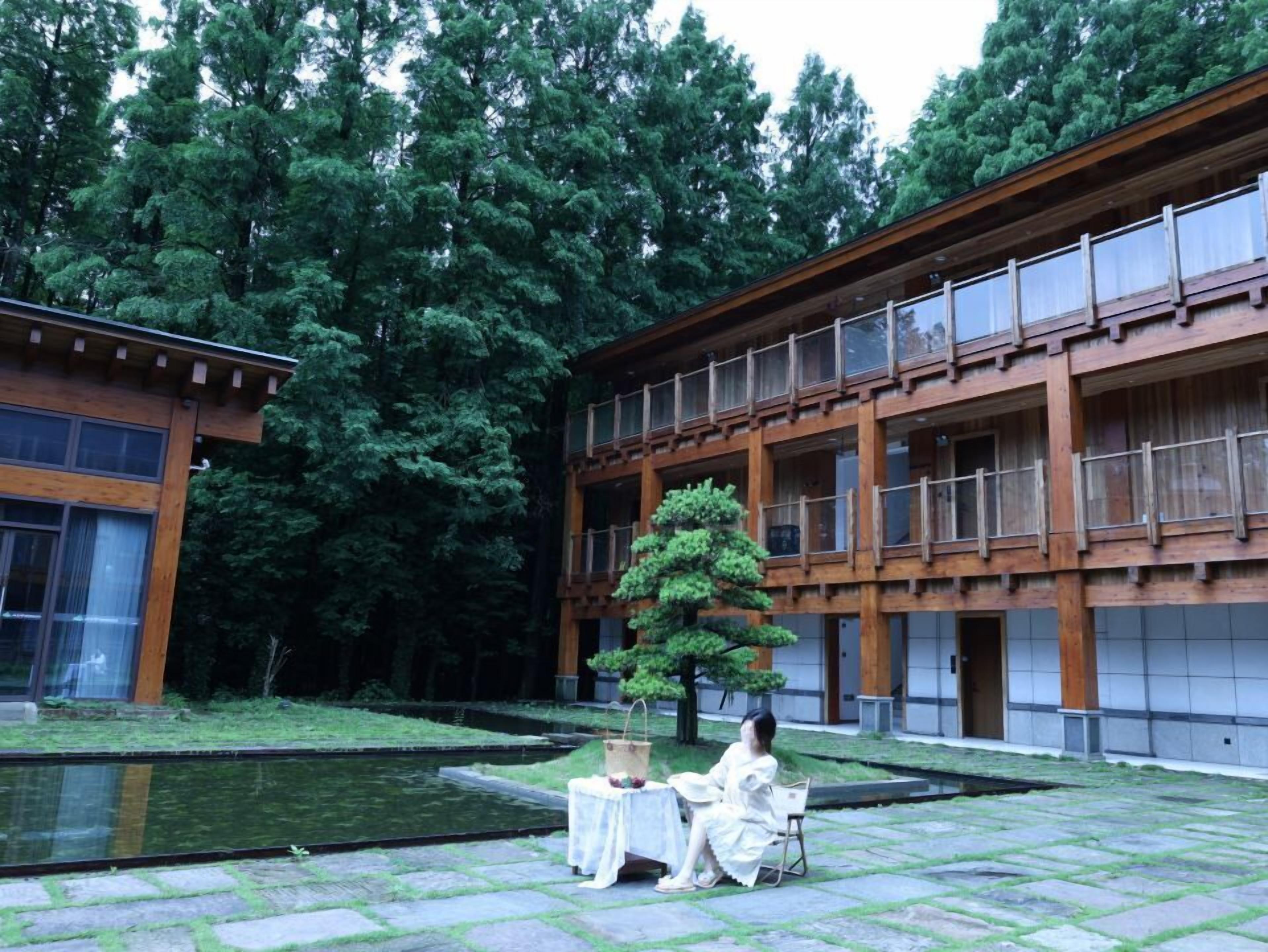 A building with a wooden exterior, a central courtyard with a water feature, and a person seated at a table.