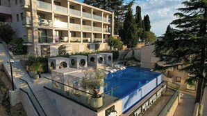 Un hotel de varios pisos con piscina en la azotea, mobiliario exterior y un jardín ajardinado.