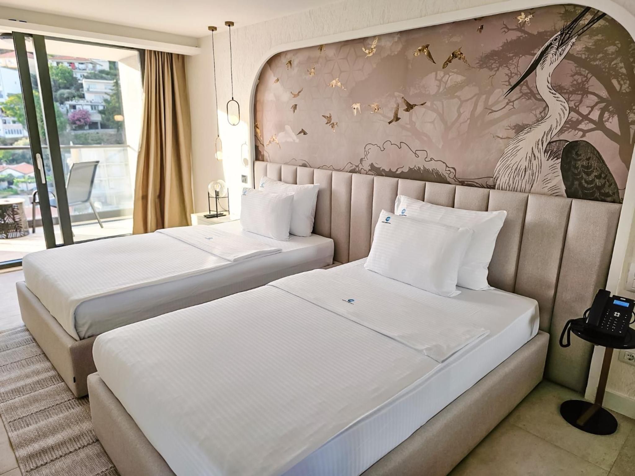 A hotel room with two beds, a large window, and a mural on the wall.