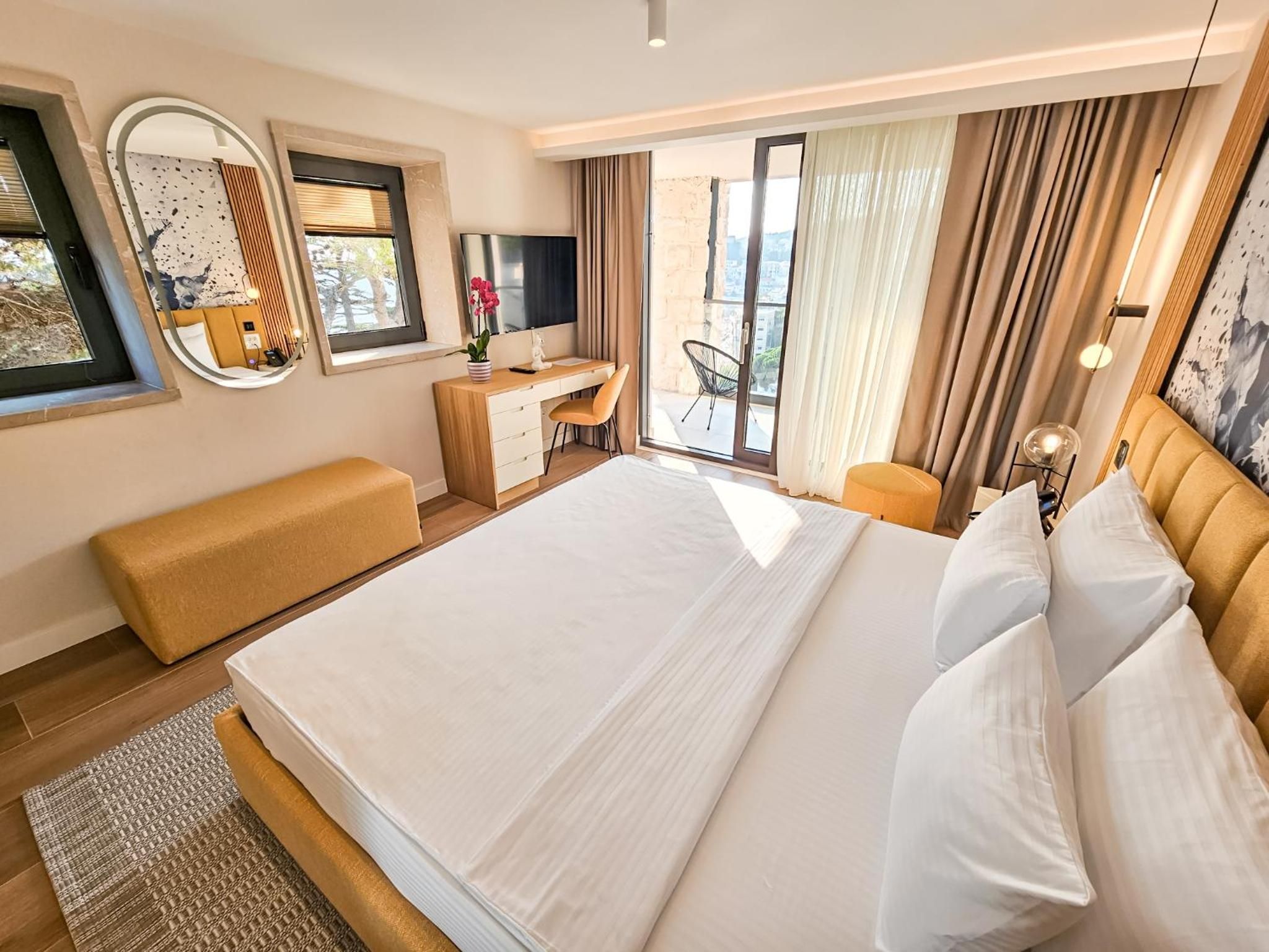 A hotel room with a large bed, a desk, a chair, a sofa, and a balcony with curtains.