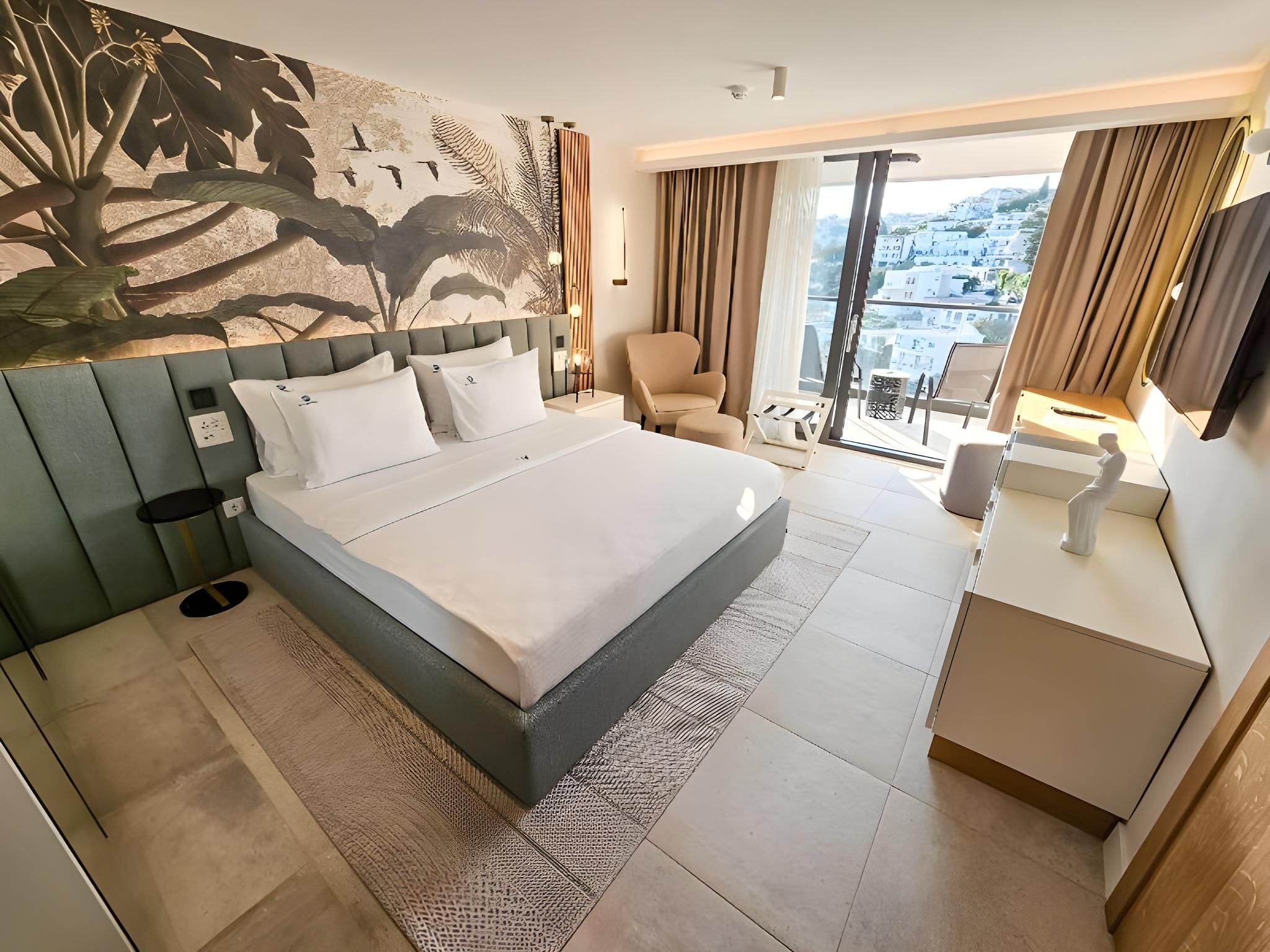 Ein modernes Hotelzimmer mit einem großen Bett, einem Schreibtisch, einem Sessel und einem Balkon mit Blick.