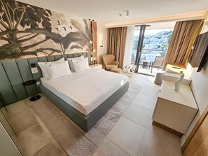 A modern hotel room with a large bed, a desk, a chair, and a balcony with a view. - The New Mediteran Hotel Villa Edition (Ulcinj)