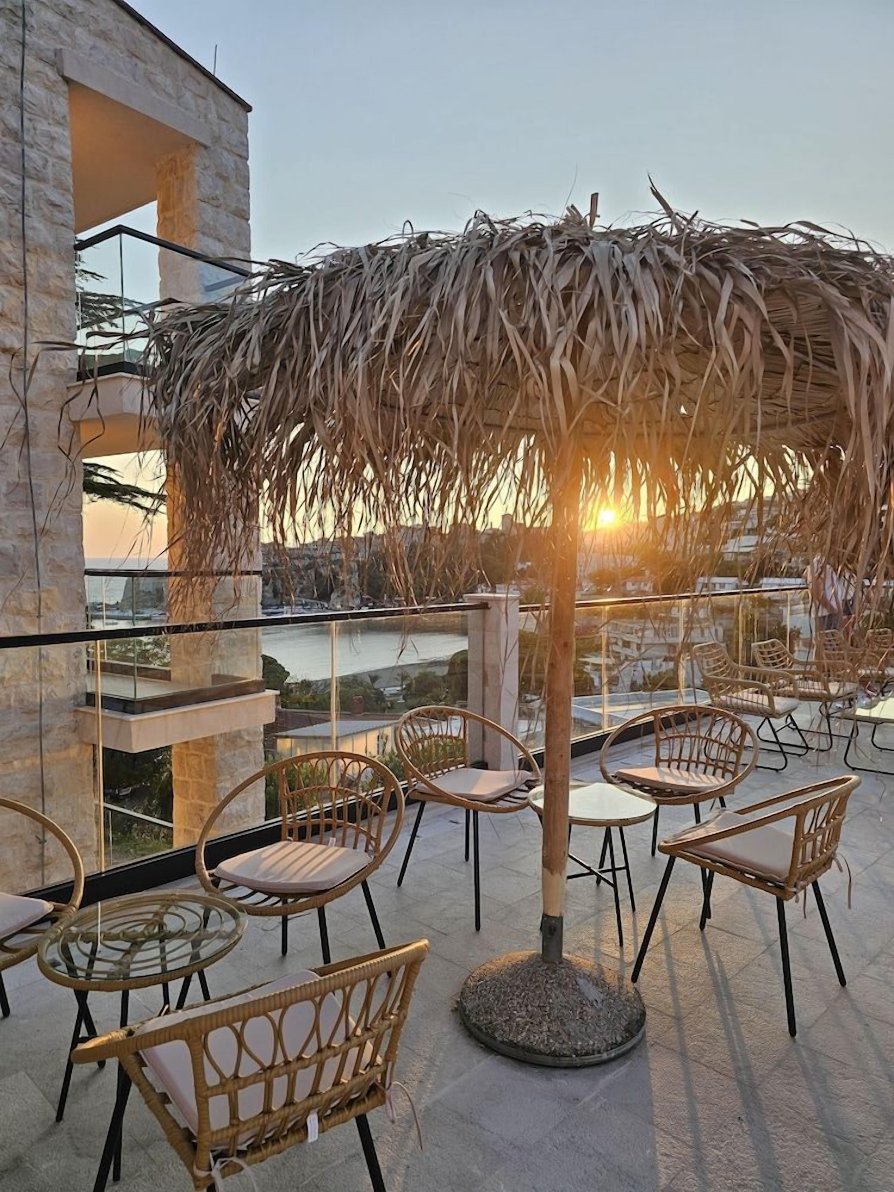 A terrace with wicker furniture and a thatched umbrella, overlooking a body of water.