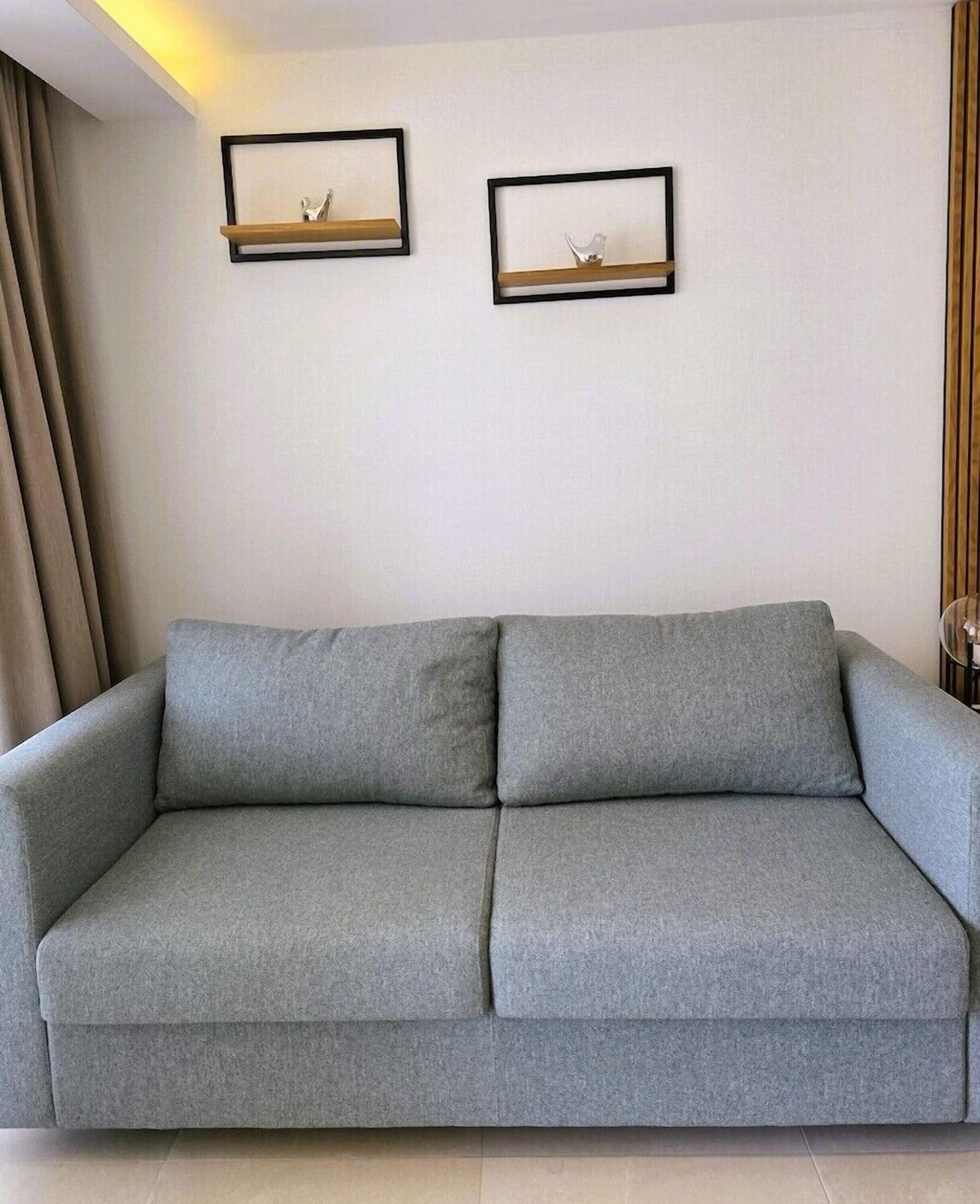 Un canapé gris, avec deux petites tables de chevet placées contre un mur uni, chacune surmontée d’un tableau encadré.