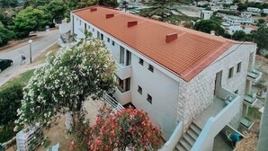 Un edificio de dos pisos con techo de tejas rojas, una escalera y vistas al mar y al paisaje circundante.