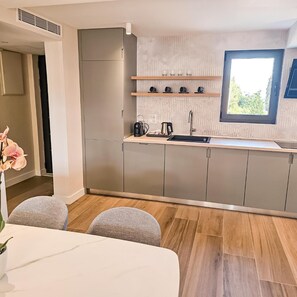 Eine moderne Küche mit grauen Schränken, einem eingebauten Backofen, einer Kaffeemaschine und einem Fenster mit Blick auf Grünflächen.