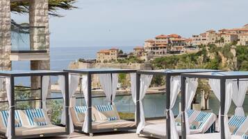 A poolside area with lounge chairs and a view of a coastal town.