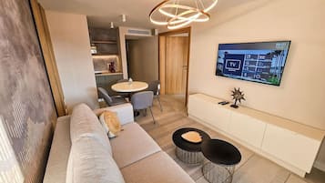 Ein modernes Wohnzimmer mit einer Couch, zwei runden schwarzen Tischen, einem an der Wand befestigten Fernseher und einer Holztür, die in einen anderen Raum führt.