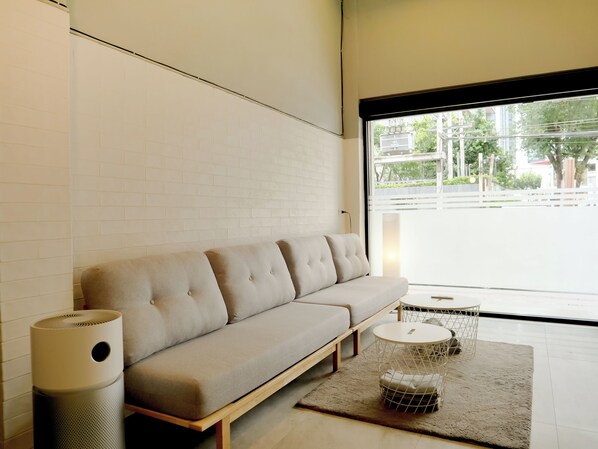 A modern living room with a sofa, a round side table, and a large window. - Jamjun Hostel Sukhumvit (Bangkok)