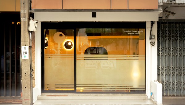 A building entrance with a glass door, a sign indicating 'Jamjun Hostel Sukhumvit,' and a visible address number '11 28.' - Jamjun Hostel Sukhumvit (Bangkok)