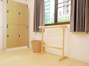A room with a wooden floor, a window with curtains, a wooden drying rack, and a wicker basket. - Jamjun Hostel Sukhumvit (Bangkok)