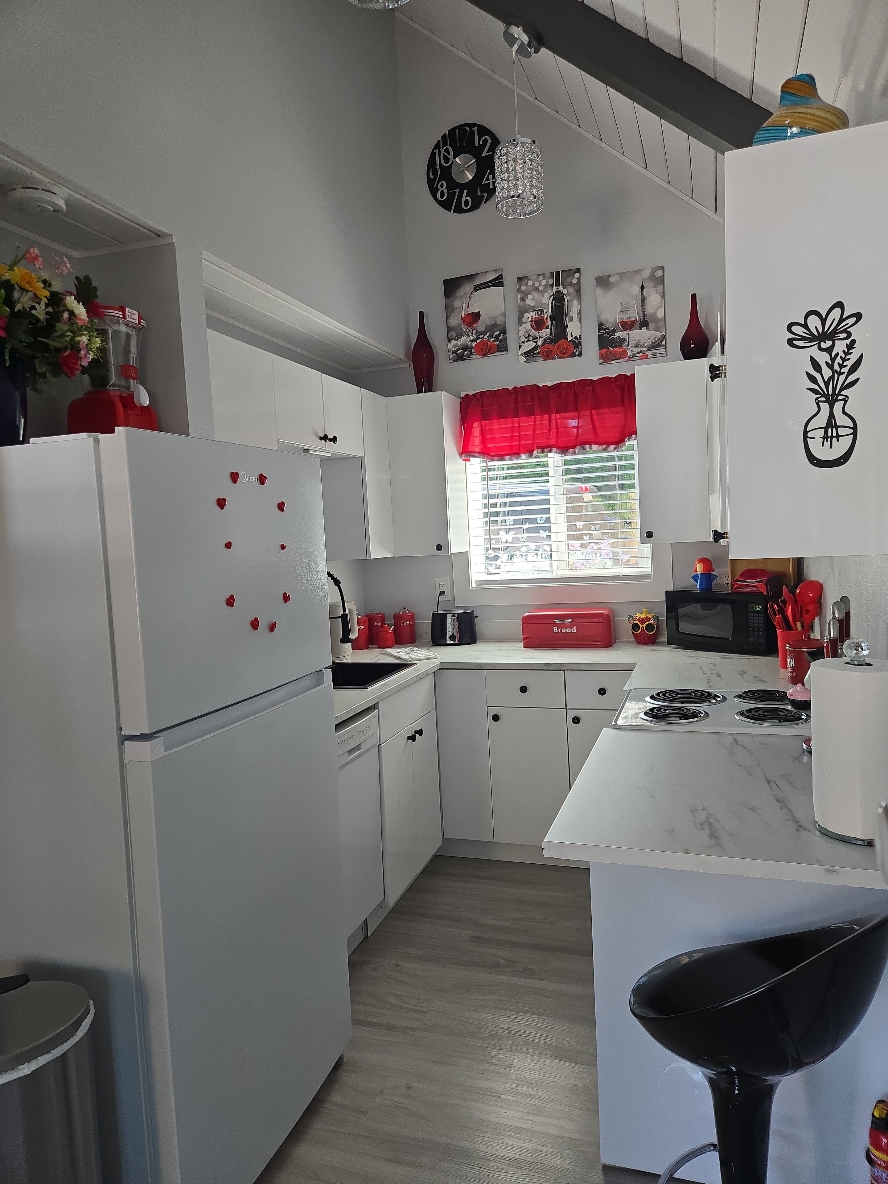 A modern kitchen with white cabinetry, a red refrigerator, a microwave, and a stove.