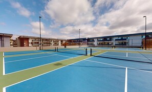 Eine Tennishalle mit mehreren Spielfeldern, umgeben von modernen Gebäuden mit Balkonen.