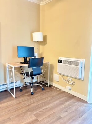 Ein Zimmer mit Schreibtisch, Stuhl, Lampe und Wand-Klimaanlage.