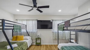 A room with bunk beds, a ceiling fan, a TV, and a small table with a lamp. - Spacious 4BR San Antonio Home w/ Private Pool, Game Rooms & Gym (San Antonio)